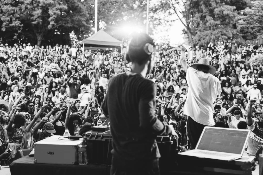 A vast outdoor festival crowd seen from behind the DJ table at SummerStage, Herbert Von King Park, Brooklyn — KAMAUU + dashMOON, black and white