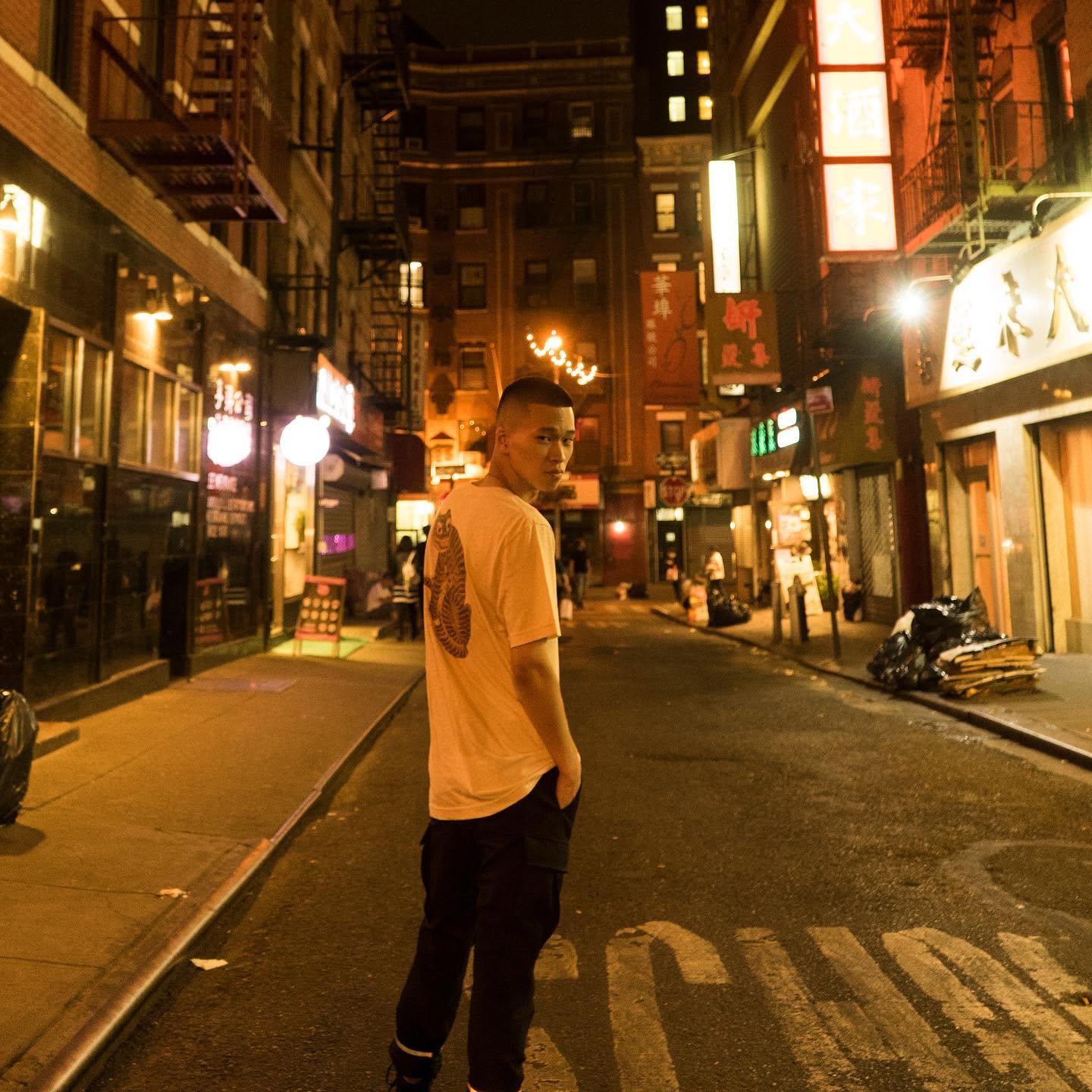 A person in a graphic T-shirt standing in a lit city street at night
