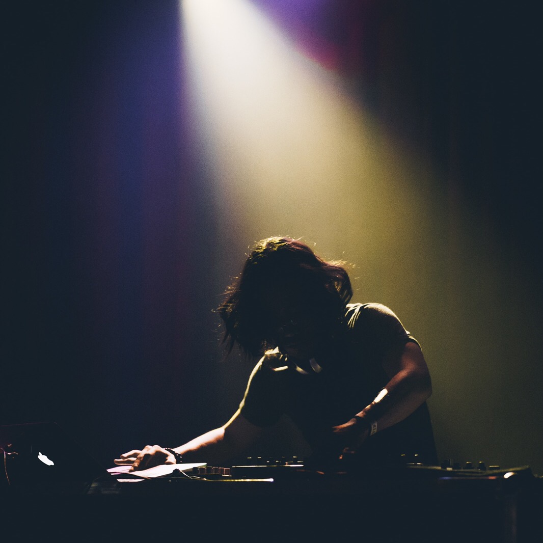 dashMOON leaning over the decks under a single dramatic spotlight in a dark room
