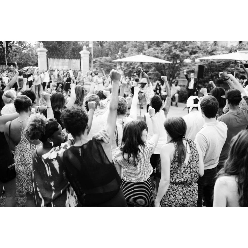 A crowd with raised fists at an outdoor performance in the Cooper Hewitt garden, black and white