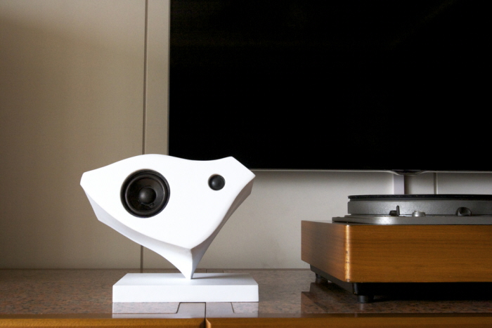 Isolated white Kardia speaker balanced on its pointed support beside a turntable