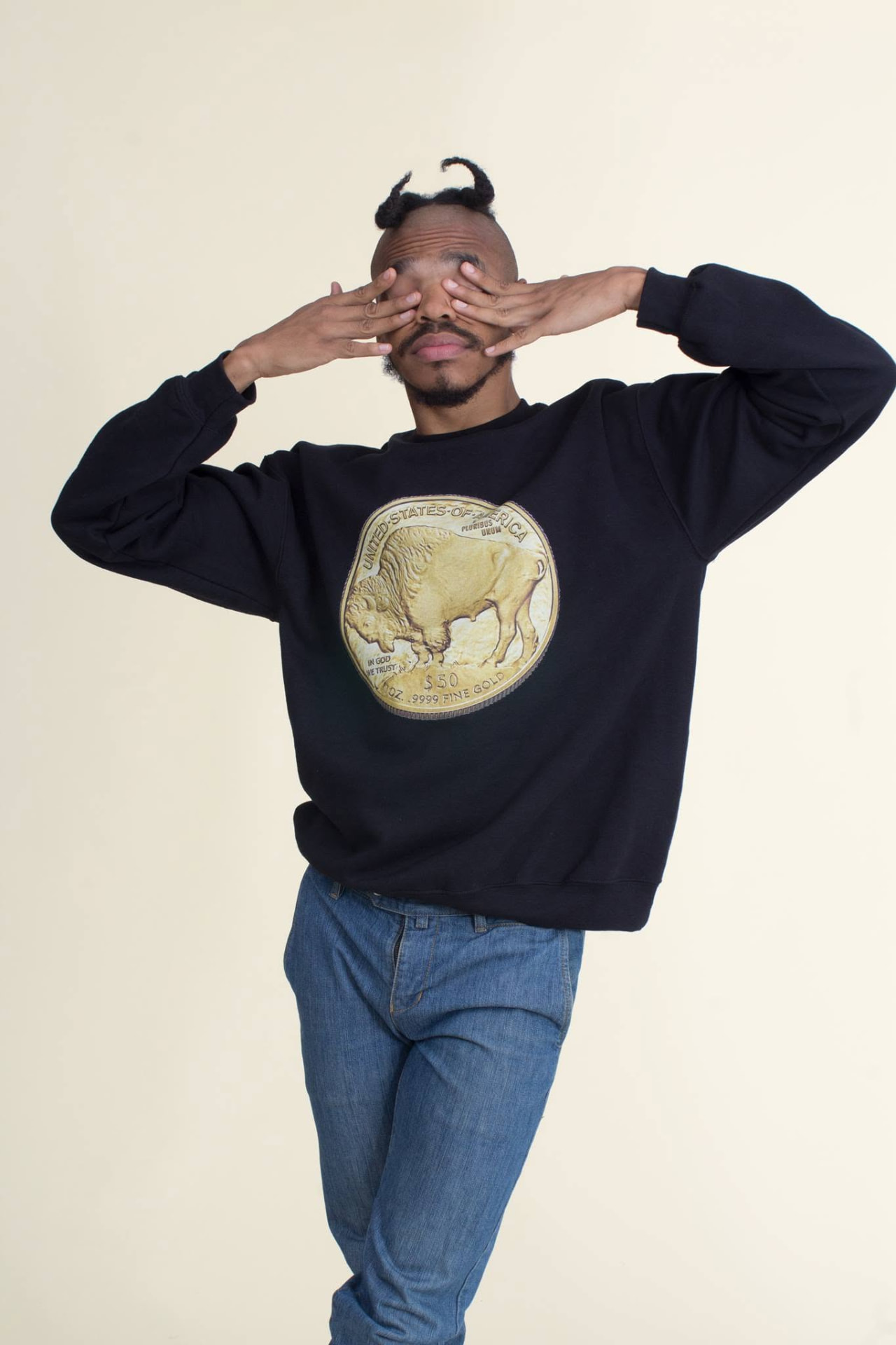 Studio portrait of a person wearing a black sweatshirt with a large gold coin graphic