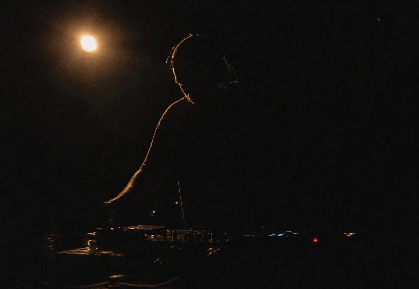 Silhouette of a figure behind a mixer under a single warm light